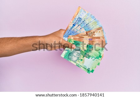 Hispanic hand holding south africa rands banknotes over isolated pink background.