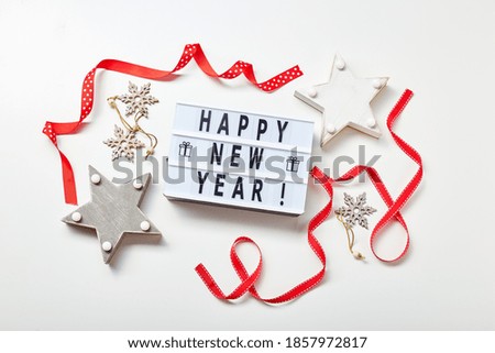 New Year or Christmas composition, flat lay, top view. Light box inscription Happy New Year, red ribbons and wooden decorations of stars and snowflakes, copy space.