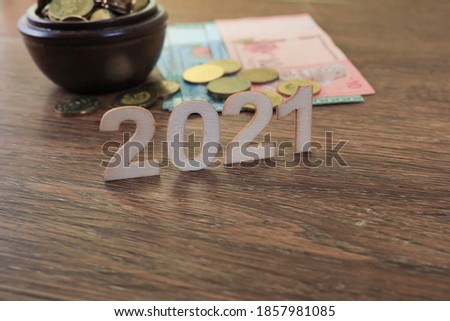 Block numbers on 2021 on wooden background with group of coins and banknotes at the back