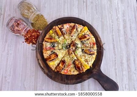 pizza in a wooden plate with chilly flakes and oregano