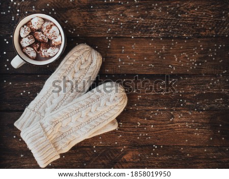 Winter flat lay with mitten and mug with hot chocolate or cocoa with marshmallow on dark rustic wooden table with silver star. Christmas and new year background. Top view, copy space. Cozy composition Royalty-Free Stock Photo #1858019950