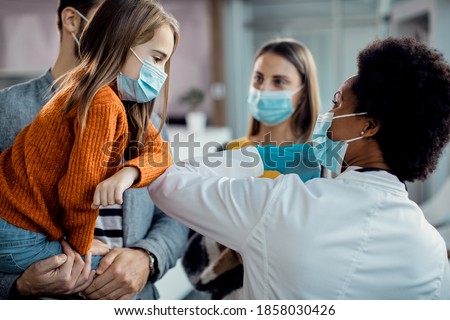 Small girl elbow bumping with a pediatrician while greeting at the clinic during coronavirus pandemic.  Royalty-Free Stock Photo #1858030426
