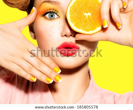Beauty Model Girl takes Juicy Oranges. Beautiful Joyful teen girl with freckles, funny red hairstyle, yellow makeup and nails. Professional make up. Orange Slices.   Royalty-Free Stock Photo #185805578