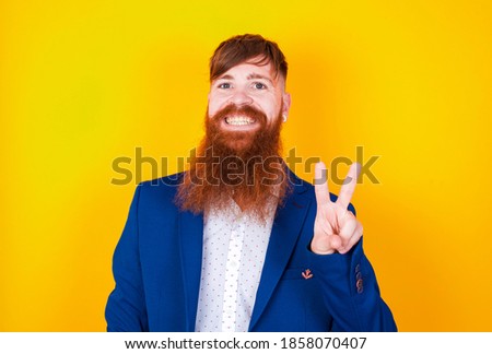 Young handsome red haired businessman standing against yellow background, showing and pointing up with fingers number two while smiling confident and happy.