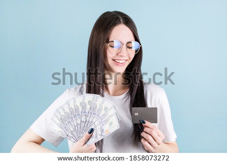 Photo of happy young woman standing isolated over blue background. Looking aside holding money and credit card.
