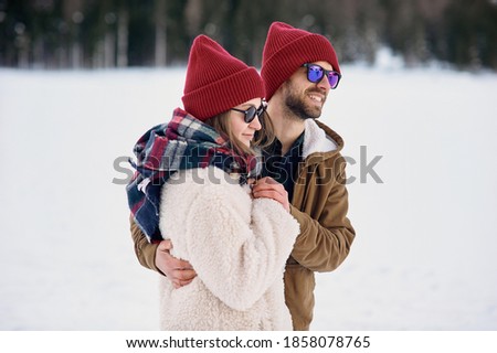 Close up of young man and woman tenderly hugging outdoors among snowy terrain.