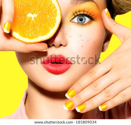 Beauty Model Girl takes Juicy Oranges. Beautiful Joyful teen girl with freckles, funny hairstyle, yellow makeup and manicure. Professional make up. Orange  Slices 