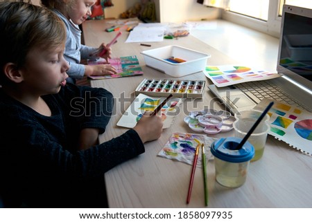 Children painting pictures with watercolor paints during art lesson. Pupils are concentrating on drawing with brush. Watercolor color wheel and palette. Color theory beginner hobby lessons