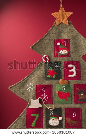 Christmas calendar with gifts for children. Textile advent calendar on paper red background. Festive winter holiday card, copy space.