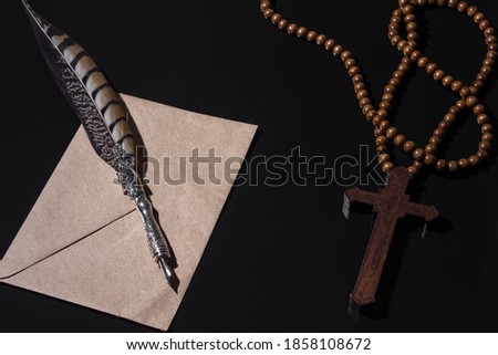 wooden religious cross and vintage Feather quill pen on black background