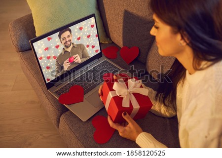 Long-distance relationship. Happy young couple talking and sending each other love on virtual date on Valentine's Day. Happy woman video calling man during lockdown and showing present she prepared Royalty-Free Stock Photo #1858120525