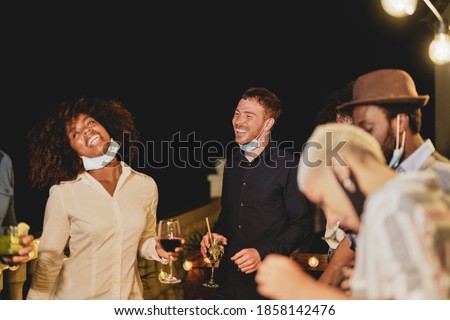 Cheerful multiracial people dance together at home on patio while wearing surgical face mask under chin - Private home party