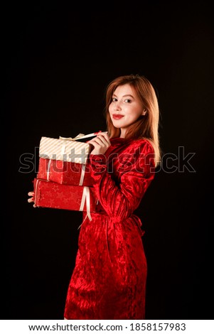 A girl in a red dress on a black background holds a gift in her hand. 