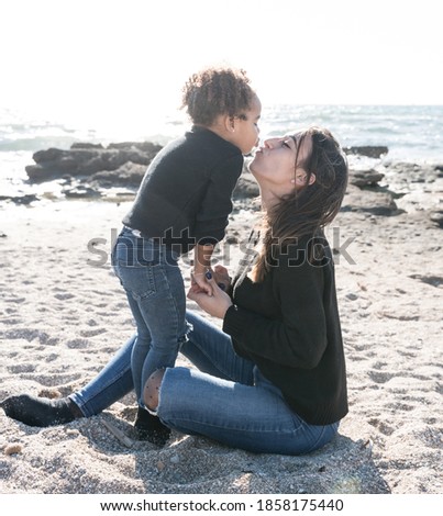 Affectionate kiss between a young mother and her African American daughter, in the sand on the beach