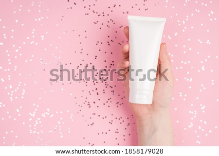 Skin care concept. Close up top above overhead view photo of female hand holding showing cream bottle over pastel pink desk background with shiny dots