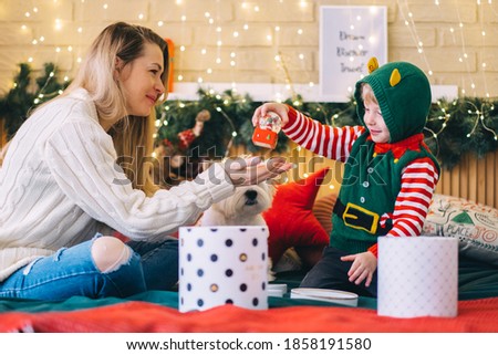 The child gives a gift to the mother. Mother with her lovely son on the background of the Christmas tree. Christmas at home. Traditions