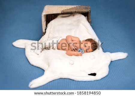 Portrait of sweet newborn baby boy lying on white fur blanket near basket. Sleeping cute newborn baby. First days of life. One week old baby.