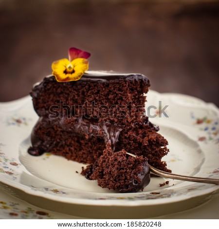 Piece of delicious rich chocolate cake decorated with a fresh pansy flower. Selective focus