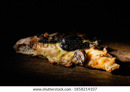 a single slice of pizza on wood and black background with mozzarella cheese, black olive, mushrooms, mushrooms and pesto córdoba argentina