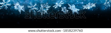 Cold winter snowflakes falling with sparkling falling snow and glittering blue background.