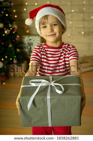 Smiling child in a red Santa Claus hat with a Christmas present on the background of a Christmas tree. New Year's magic. Christmas concept.