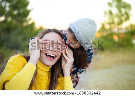 Happy young girl laughing, covering eyes of her mother with her hand. Adorable little girl surprising her mother