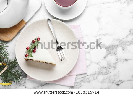 Slice of traditional Christmas cake decorated with rosemary and pomegranate seeds served on white marble table, flat lay. Space for text