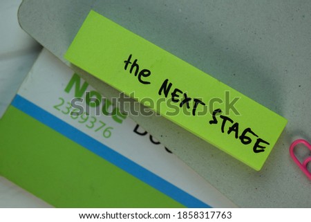 The Next Stage write on sticky note isolated on Wooden Table.
