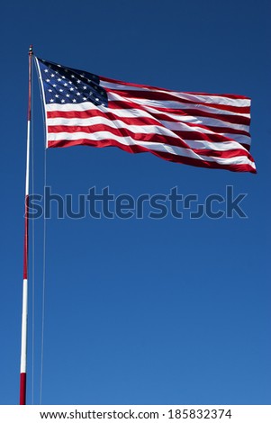 American flag on a pole blowing in the breeze with blue sky in the background.