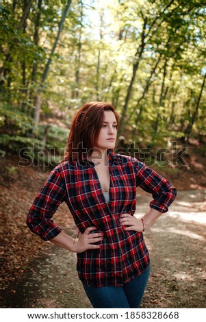 traveler hipster woman standing alone in autumn woods in checkered shirt and blue jeans . Cold weather, fall colors. Wanderlust concept.