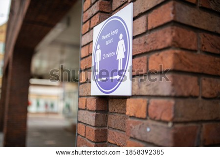 Blue sign requesting people to keep a safe distance of 2 meters on brick wall. Red brick column with social distancing sign. Health measures against covid-19