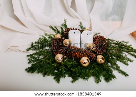Scandinavian christmas card with white fabric and christmas wreath with white candles inside. Green fir branches, pine cones, golden balls and candles on white background with space for text.