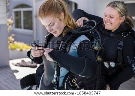 Scuba dive buddies helping each other to put on their BCDs. Royalty-Free Stock Photo #1858405747