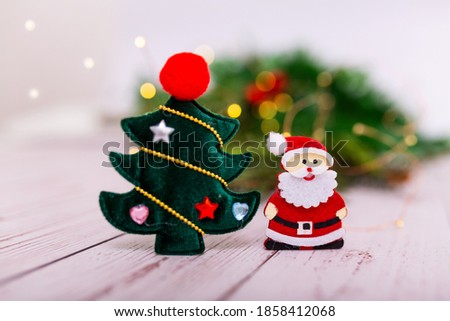 Green velvet Christmas tree pendant with a Santa Claus decoration on a background of bokeh Christmas garlands and Christmas tree. Christmas tree decoration close-up