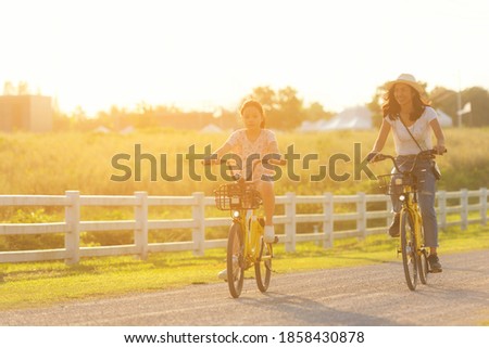 Mother and daughter with bicycling at the garden meadow in sunset near white fence.  Lifestyle Family Concept
