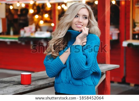 Smiling beautiful woman drinks mulled wine outdoors with christmas lights.