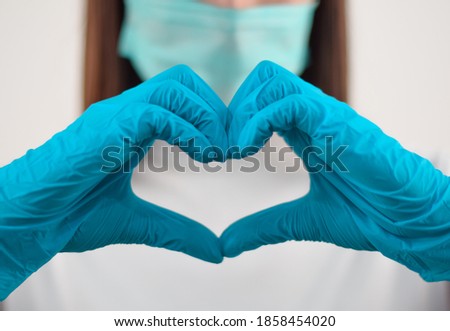 Woman with a medical mask and hands in latex glove shows the symbol of the hear