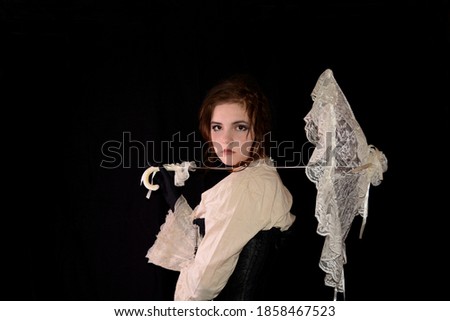 Young girl in steam punk look, holding white open umbrella made of lace, standing in front of a black background  and copy space