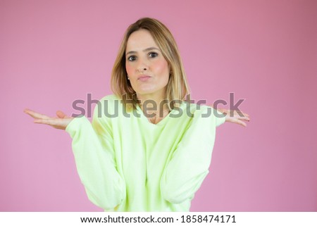 Young woman standing over pink isolated background clueless and confused expression with arms and hands raised. Doubt concept.