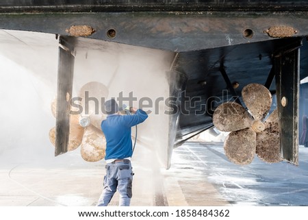 Man power washing the hull and propellers of a superyacht after haul out for shipyard period, with water spray causing a mist/haze in the air Royalty-Free Stock Photo #1858484362