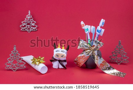 toy dental model, toothbrushes in a vase with a gift ribbon, symbol of the year and toothpaste on a red background