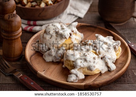 Biscuits and creamy sausage gravy on a wooden plate with fried potatoes in background Royalty-Free Stock Photo #1858530757