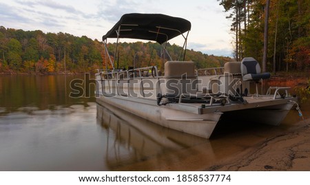 Pontoon boat beached on the shore of Falls Lake in Autumn Royalty-Free Stock Photo #1858537774