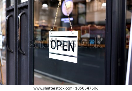 An open sign hanging on the black metal frame glass door in front of the cafe and coffee shop. Sign open now concept. Royalty-Free Stock Photo #1858547506