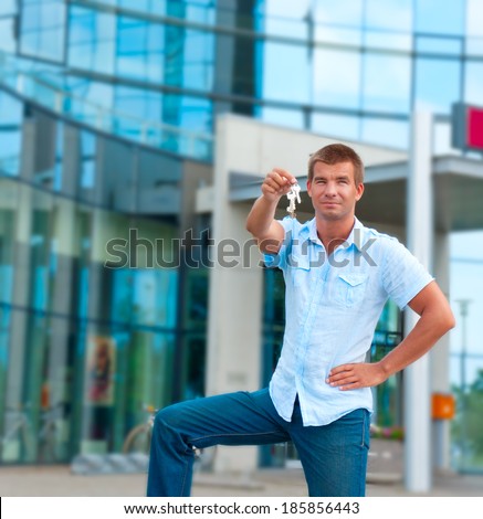 business man holding a key in front of modern business building.