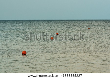 calm water surface where orange buoys float with round shapes marking the safety zone for riders and sailors