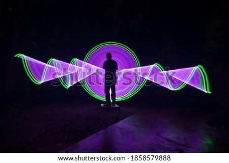 One person standing alone against beautiful green and purple circle light painting as the backdrop