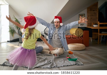 little girl running into dads arms with santa hat. christmastime