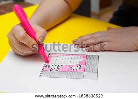 A woman is solving a Japanese crossword puzzle. Japanese crossword puzzle on yellow background