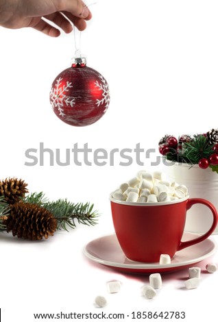 Red cup with marshmallows. Christmas red ball in hand and fir branches on a white background. Christmas concept. Christmas. Isolate. Copyspace